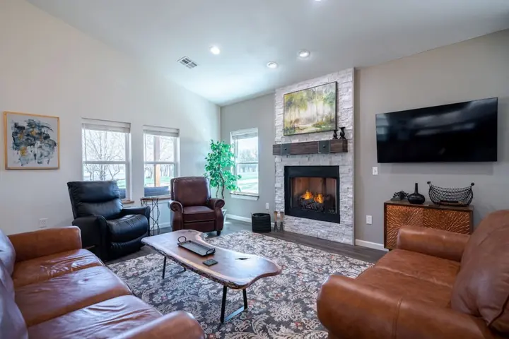 Living room with leather sofas and recliners around a lit stone fireplace
