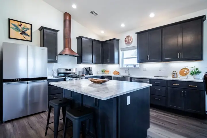 Kitchen with dark cabinets, a copper range hood and a marble-topped island