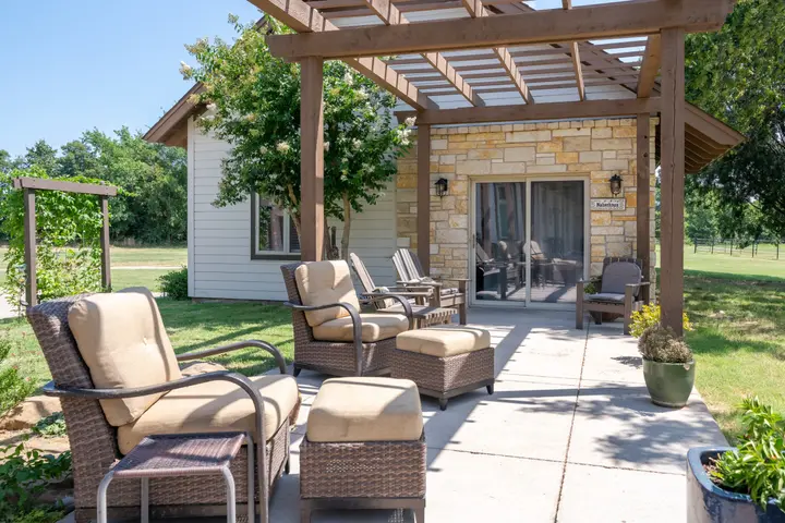 Cottage exterior: cushioned wicker lounge chairs and ottomans on a pergola-covered breezeway patio, a quiet spot to unwind outdoors