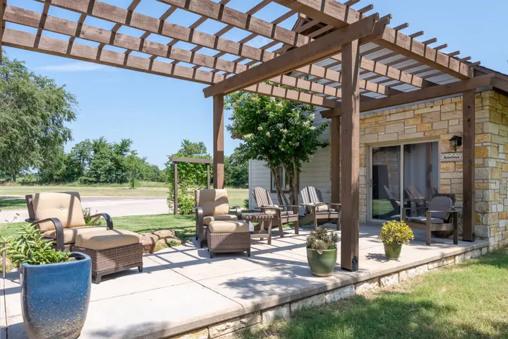Cottage exterior: Adirondack chairs and wicker seating on the pergola-covered patio, with open lake and country views
