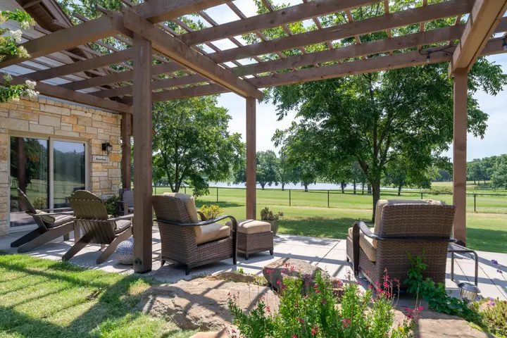 Cottage exterior, lakefront views from a pergola covered patio with Adirondack chairs looking out over a peaceful parklike setting