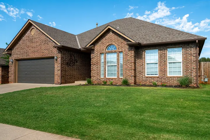 Red brick single-story house with a two-car garage and a green front lawn