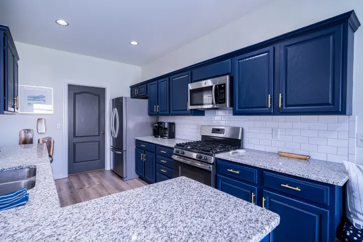 Kitchen with navy blue cabinets, granite counters, gas range and subway tile