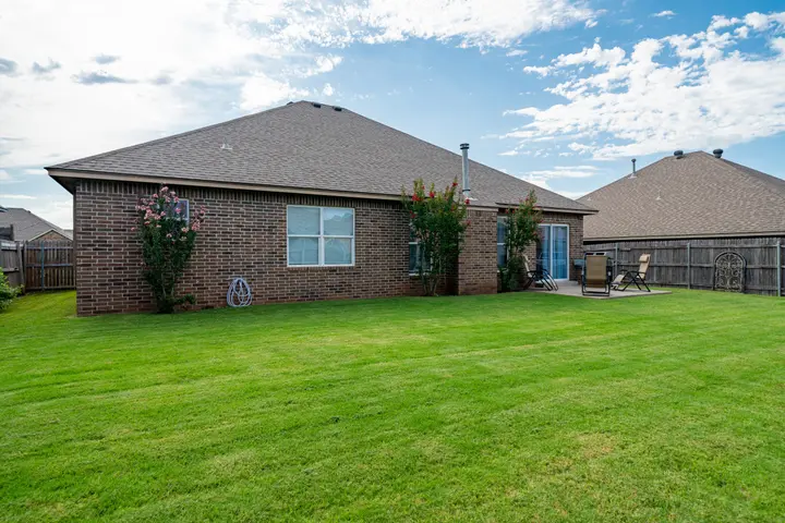 Backyard lawn and patio behind the brick house, with a privacy fence