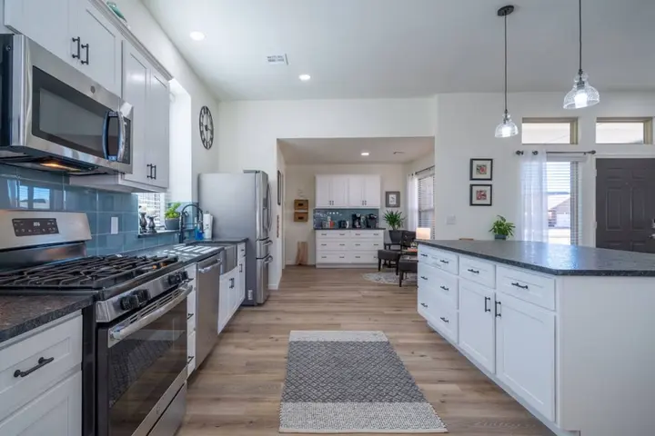 Kitchen with white cabinets, gas range, stainless appliances and a long island under pendant lights