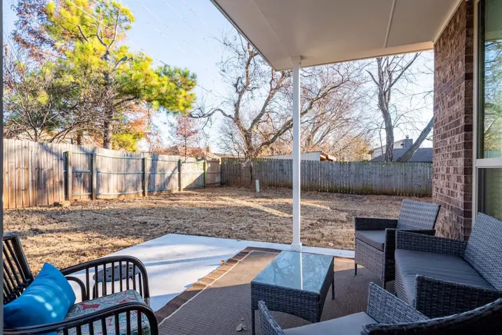 Covered back patio with wicker seating overlooking a fenced yard