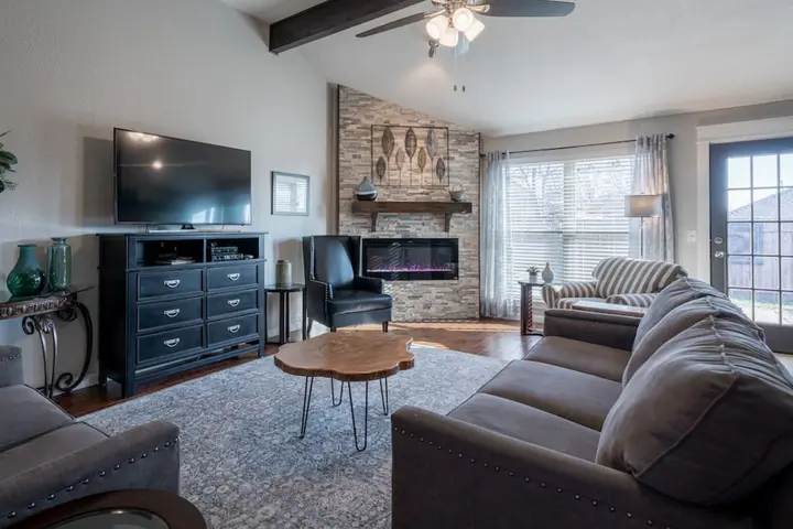 Living room with a stone corner fireplace, grey sofas and doors to the backyard