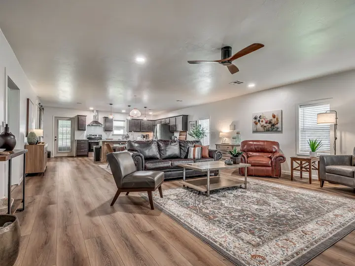 Open-plan living room with leather sofas, a large rug and the kitchen beyond