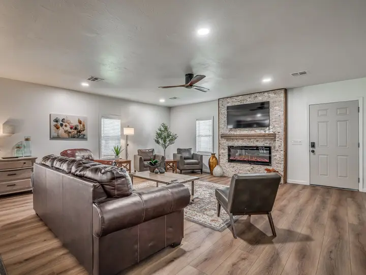 Living room with a leather sofa and armchairs facing a stone-wall electric fireplace