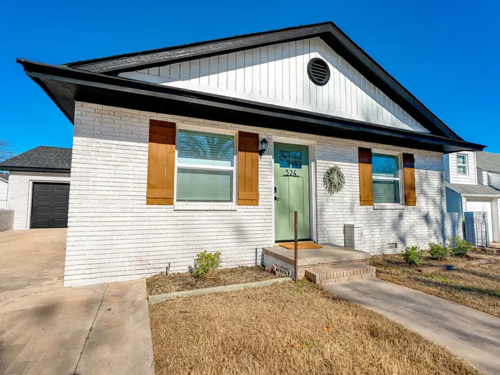 Front steps lead up to the sage green door of the freshly updated white brick cottage, a warm welcome for your family or group