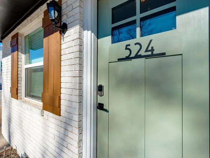 The sage green front door with its keypad lock beside a shuttered window, so you can let yourselves in with ease