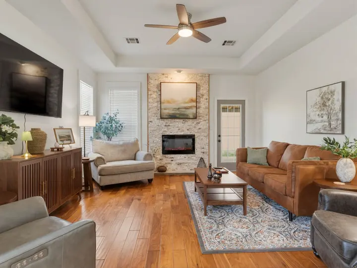 Living room with wood floors, a tiled electric fireplace and a tan leather sofa, comfortable seating for the whole group to settle in together