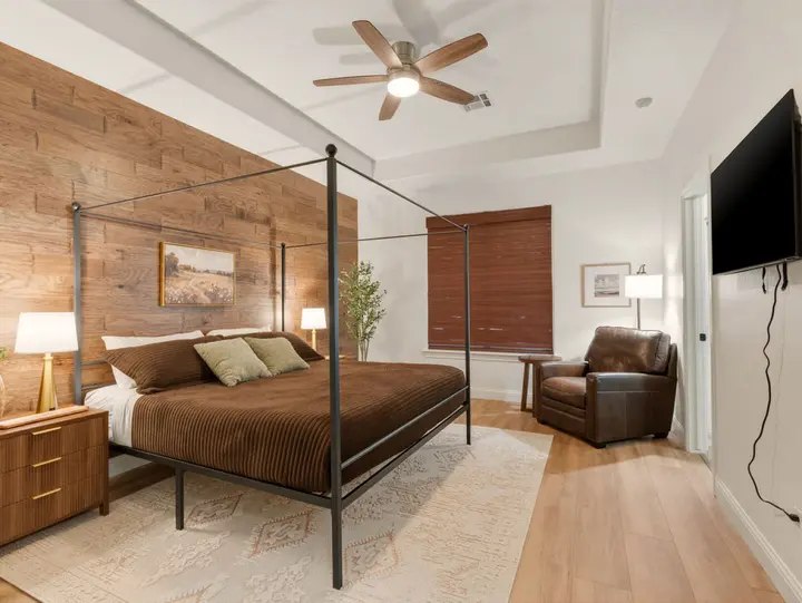 Bedroom with a wood-plank feature wall, four-poster king bed and leather armchair, a restful place to end the day on a comfortable bed