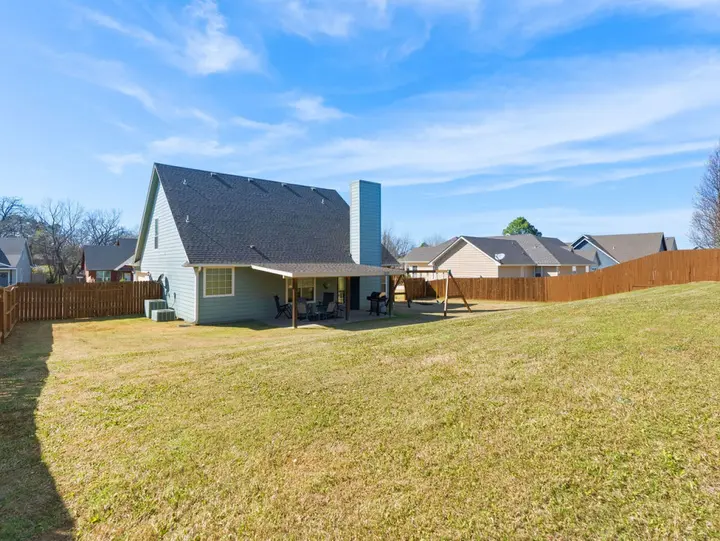Large fenced backyard lawn behind the house, with a covered patio and a swing set, plenty of room for dogs and kids to run
